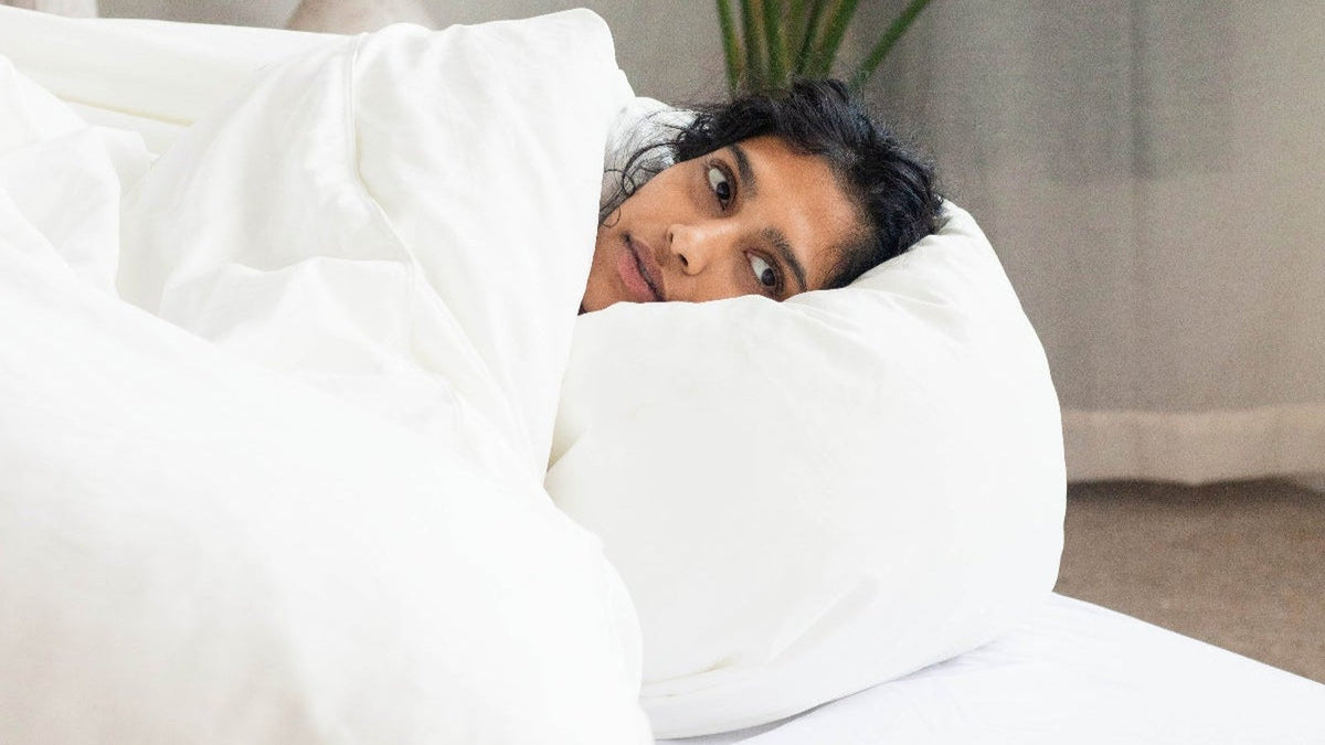 Woman peeking over the edge of a fluffy white duvet
