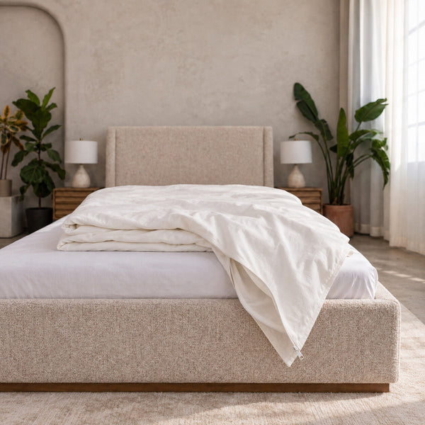 Cloud Duvet Cover in white cotton percale, loosely folded over the foot of an upholstered bed