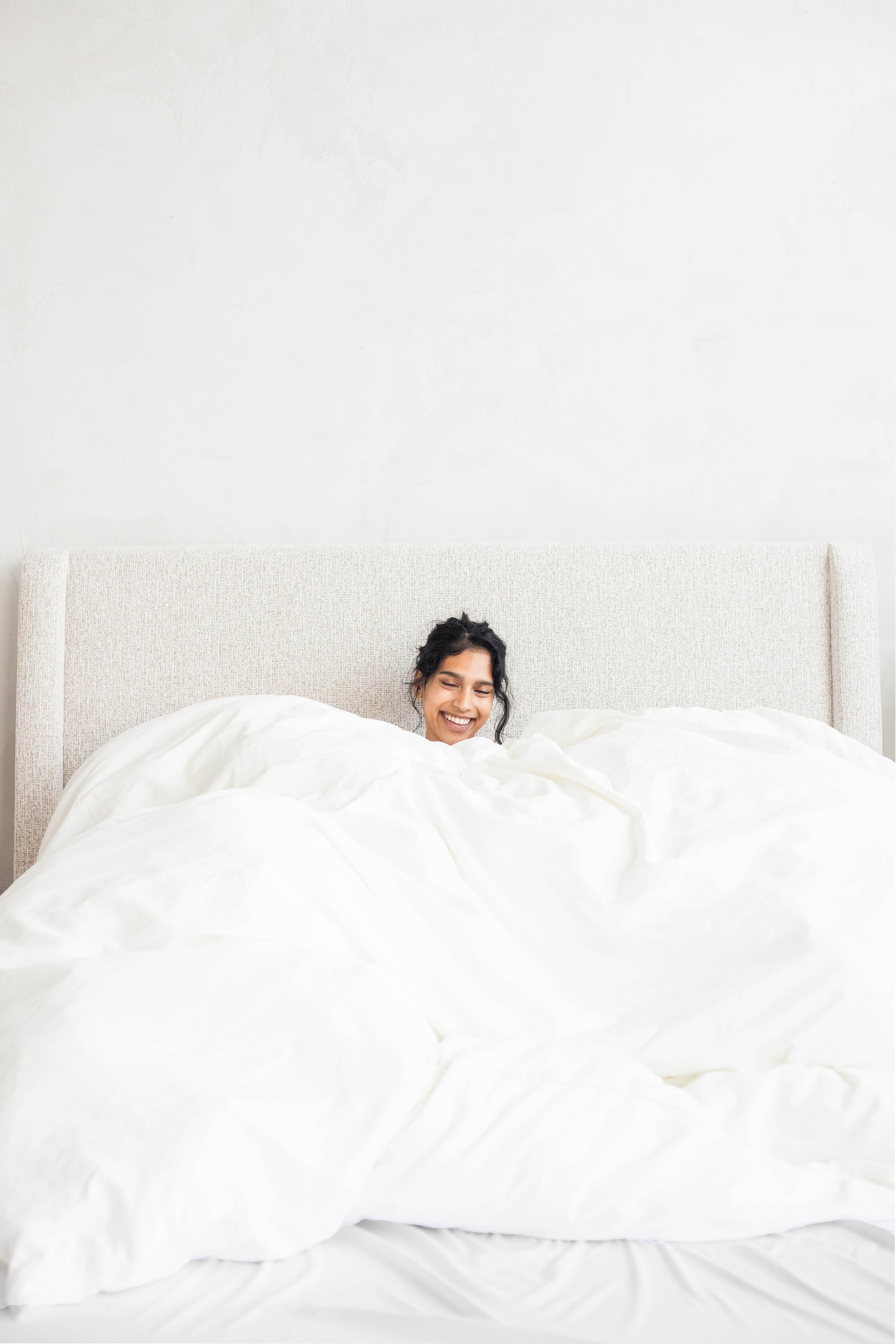 A woman smiling under a full white duvet