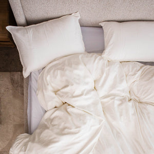 Two Cloud Pillows at the head of a bed, seen from above, with a white duvet pulled up below them