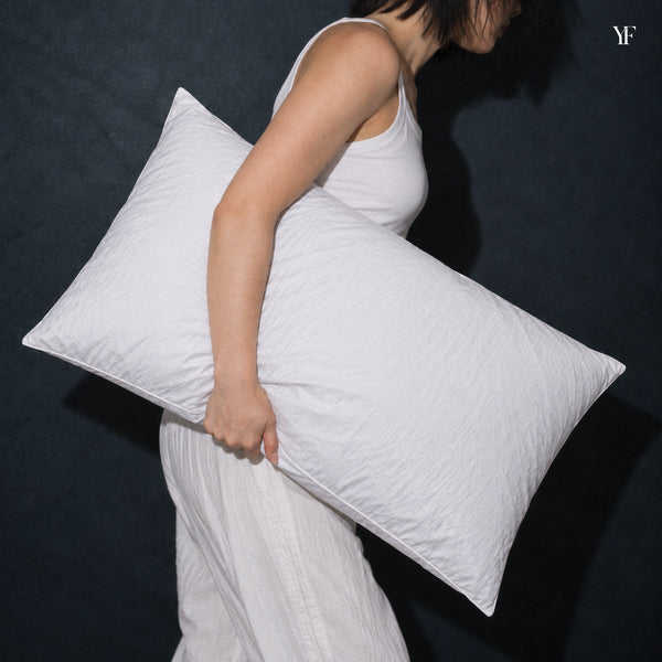 A woman carries a full white Cloud Pillow under her arm against a dark wall