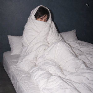 A woman wrapped head to toe in the Air duvet and its white cotton cover, sitting up in bed