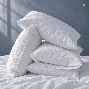 Four Royal goose down pillows in white cotton pillowcases, stacked on a bed in window light
